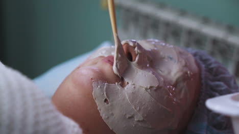 beautician applies alginate mask onto girl face with spatula