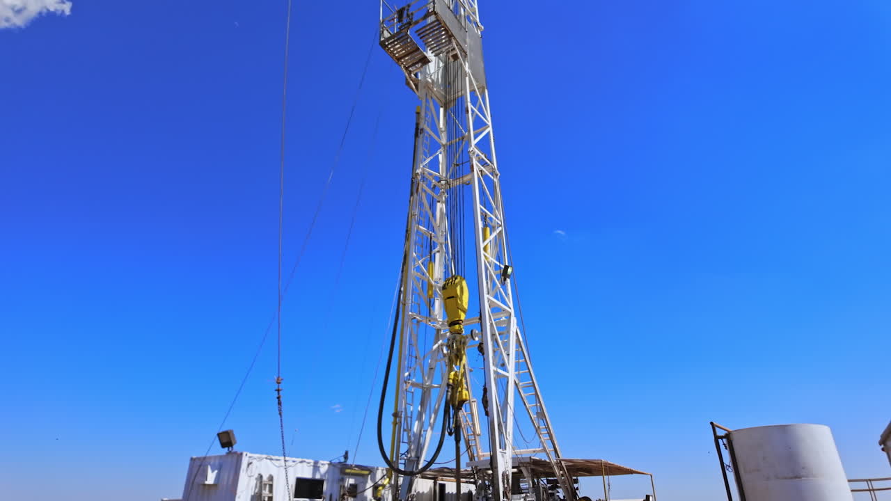 Rusty metal pipes near the tower for drilling oil. Borer attached to a high derrick works rotating. Low angle view.