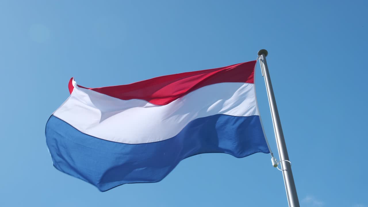 네덜란드의 빨간색, 색 및 파란색 발이 은 날 배경에 파란 하늘과 함께 바람에 흔들리고 있습니다.