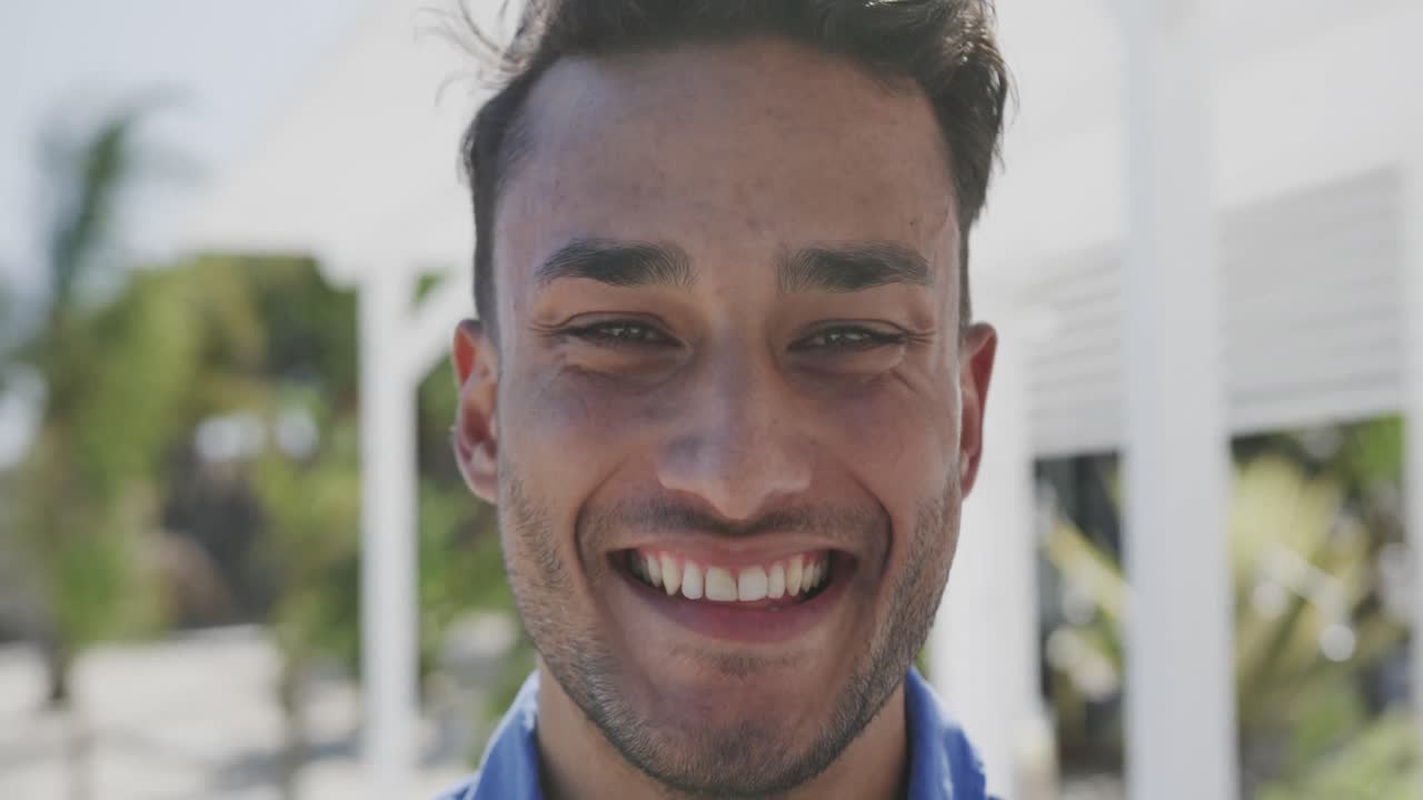 retrato de un hombre biracial feliz sonriendo en una playa soleada, en cámara lenta