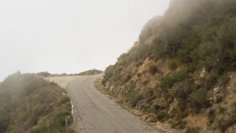 Drone-view-of-winding-road-on-side-of-mountain-obstructed-by-clouds