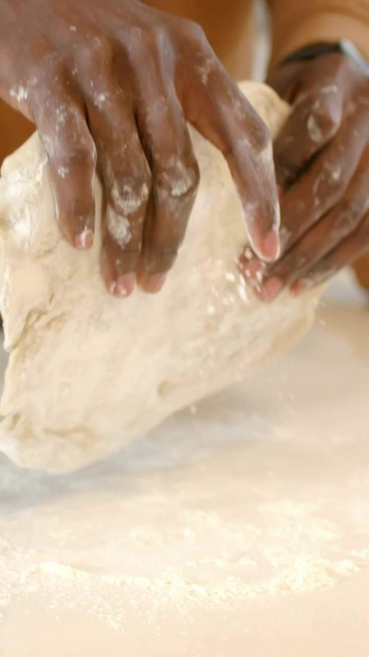 Vertical video: Pressing dough on home counter, couple in tan, green kneading to bake, flour jar