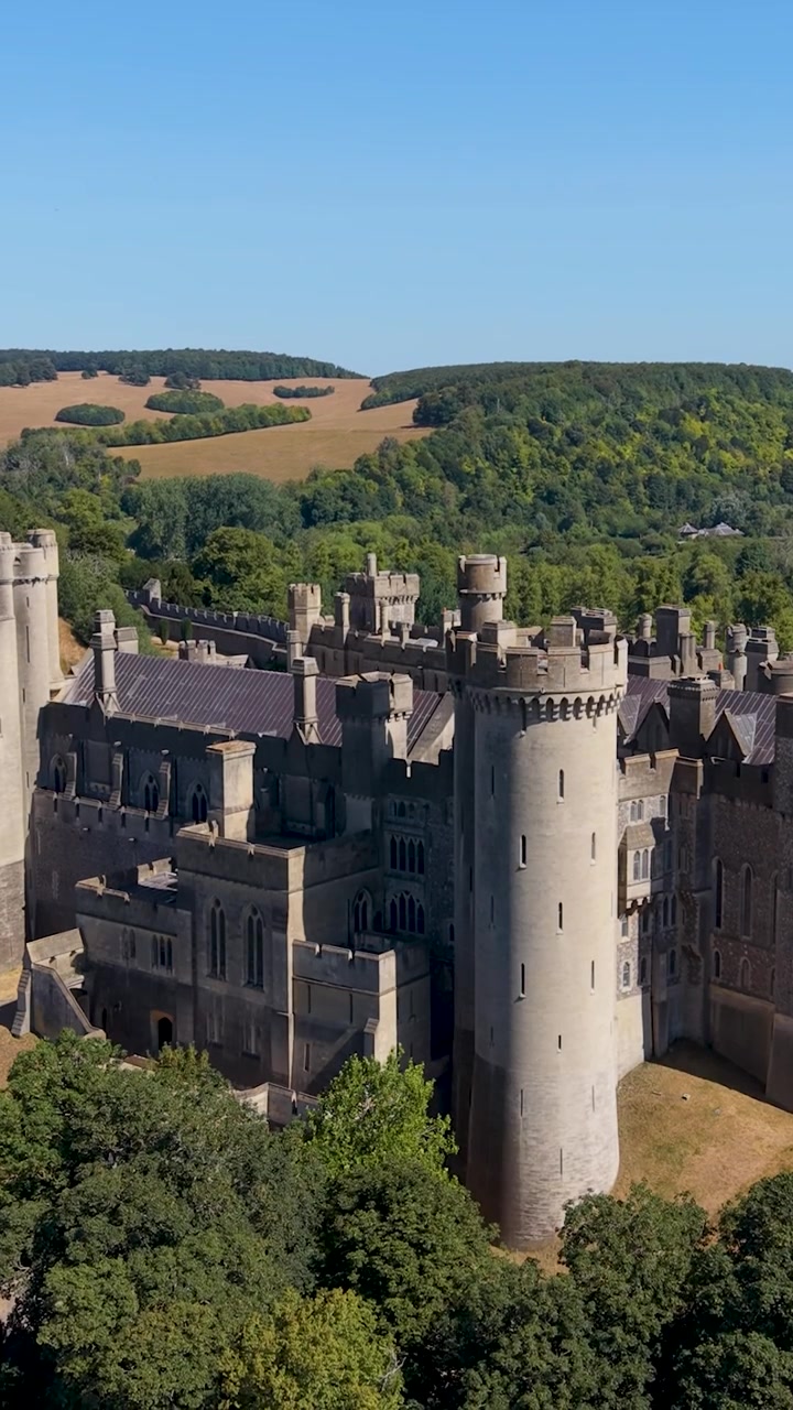 Descida aérea do Castelo de Arundel, vista de estabelecimento revelando torres medievais, muros de pedra e o parque circundante em West Sussex, Inglaterra, em um dia de verão ensolarado. Formato vertical