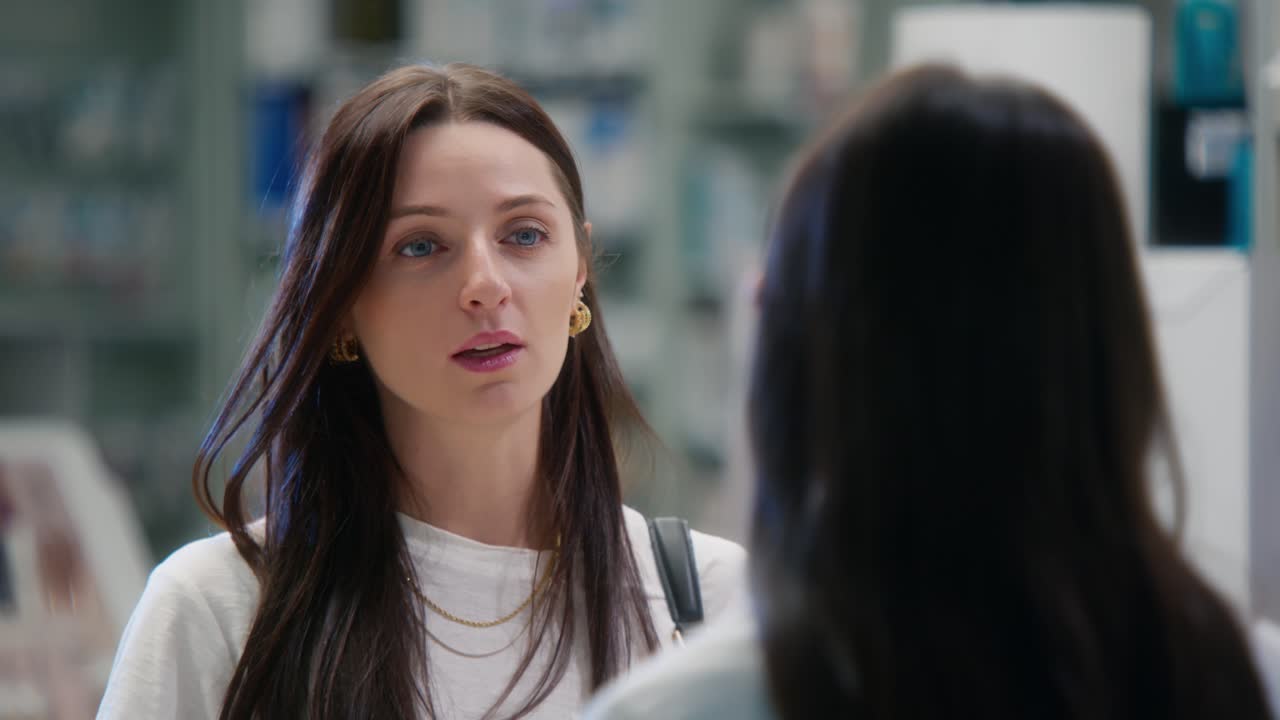 Young woman speaks to pharmacist inside a bright, modern pharmacy, captured in close-up from the counter