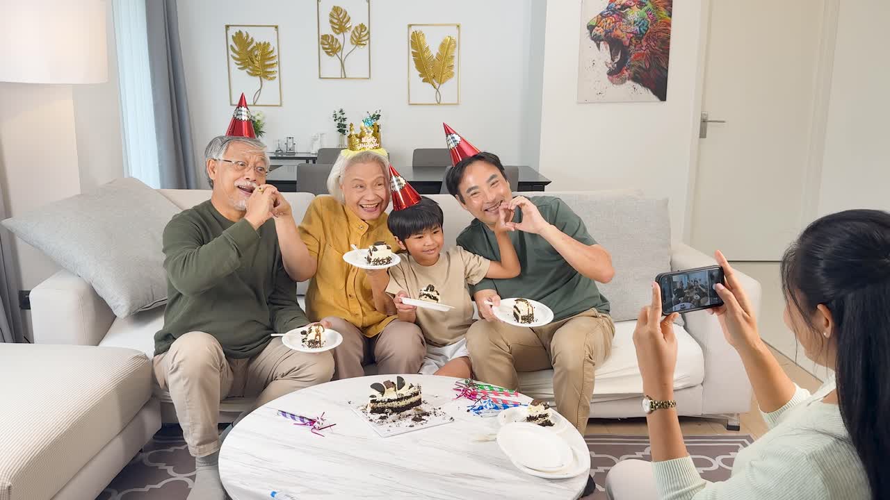Three generations celebrate with birthday cake and photos, smiling together in a bright living room