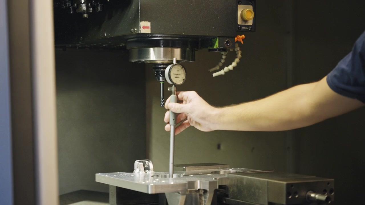 Calibrazione del punto zero di un comparatore su un pezzo metallico in un'officina di fabbrica, che mostra l'impostazione di precisione, l'attrezzatura di lavorazione, l'ago del calibro, il controllo della tolleranza e il processo di controllo qualità
