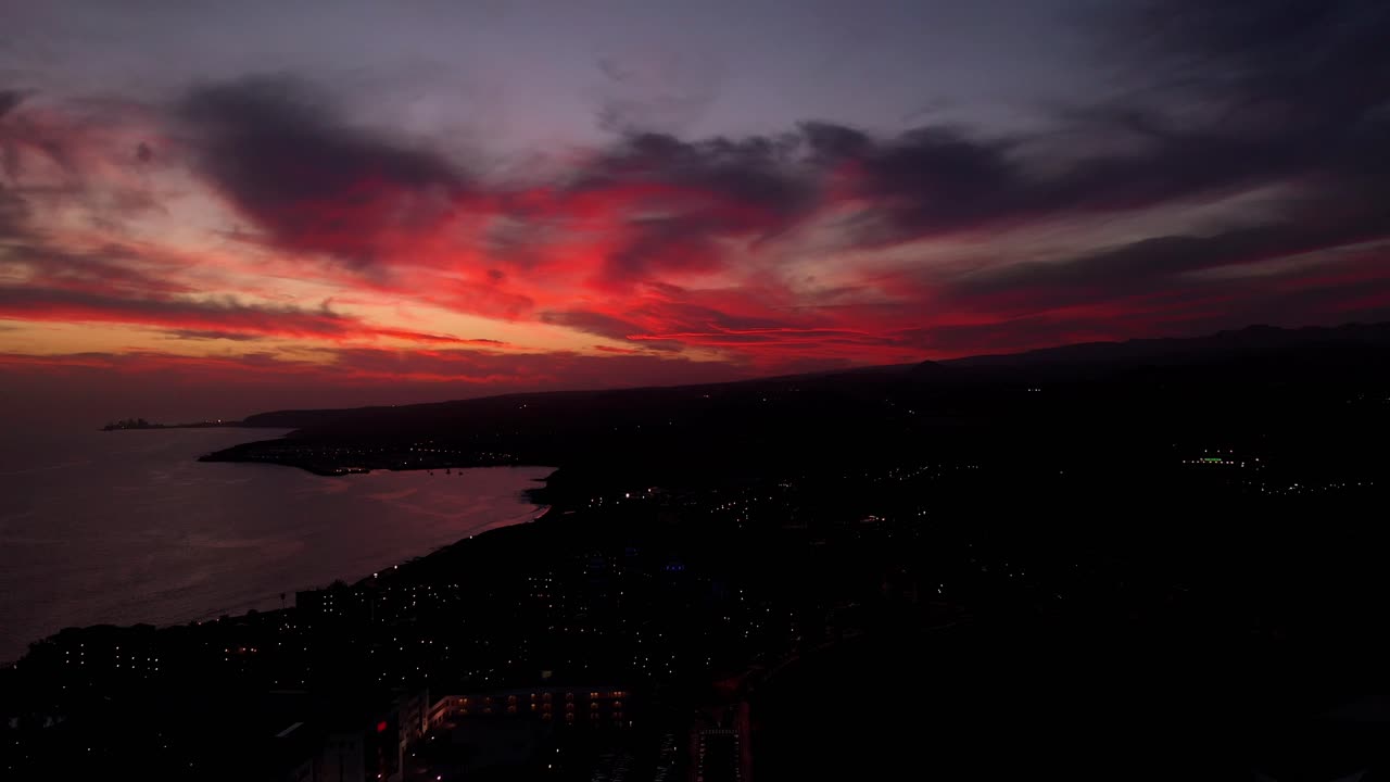tilt and move Las Palmas Gran Canaria at nightfall with vibrant red clouds, aerial drone at sea