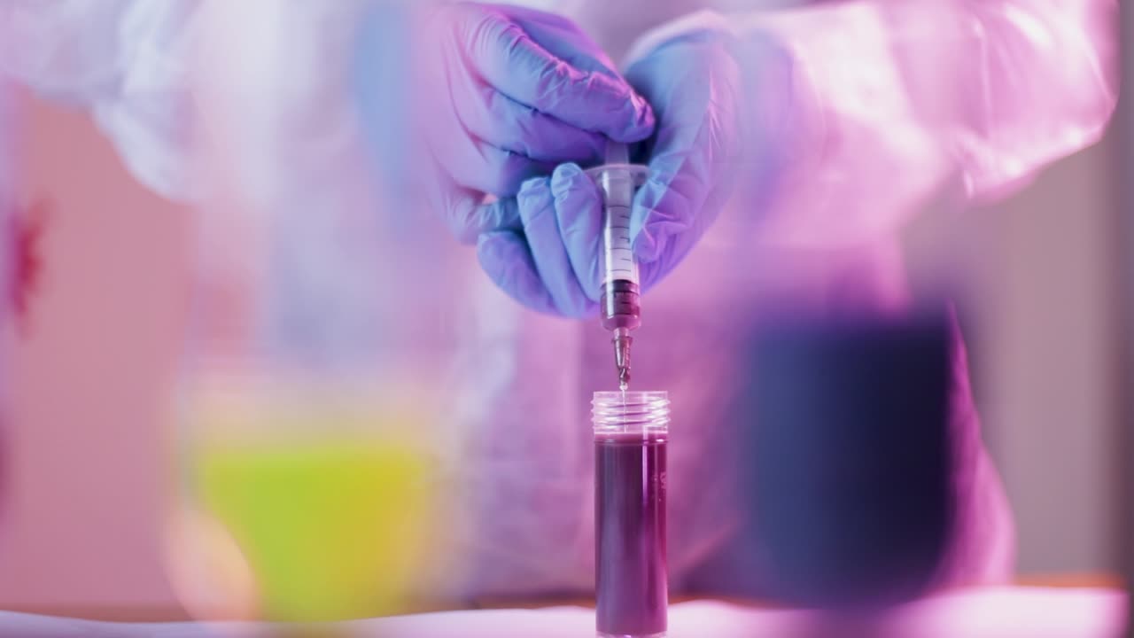 Hands of scientist absorbing red liquid solution from glass tube container by a syringe for Coronavirus test analysis