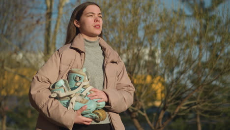 close-up of a girl walking on a sunny day while holding a skateboard. she is wearing a peach jacket and a grey inner shirt, gazing thoughtfully at the skateboard as she walks