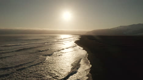 Glacier-View-By-The-Black-Beach-In-South-Iceland-With-Sun-Low-In-Horizon---wide-aerial-drone