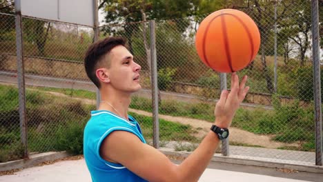 Retrato-De-Un-Joven-Jugador-De-Baloncesto-De-Aspecto-Serio-Haciendo-Girar-Una-Pelota-De-Baloncesto-En-El-Campo-De-Juego-De-La-Calle.-Tiro-En-Cámara-Lenta