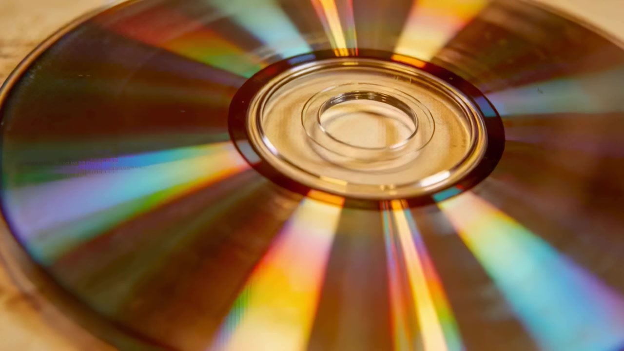 En roterende kompakt disk afslører skiftende regnbuebånd på et varmt træbord, udløst af et kameraskub.