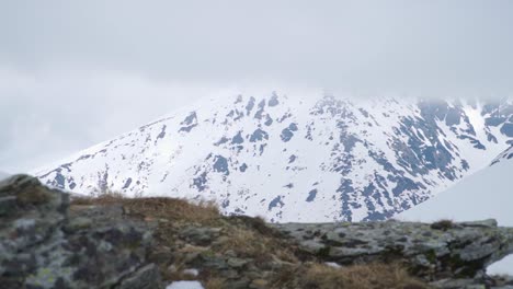 Terreno-Montañoso-Rocoso-En-Primer-Plano-Y-Acantilados-Y-Picos-Cubiertos-De-Nieve-En-Segundo-Plano