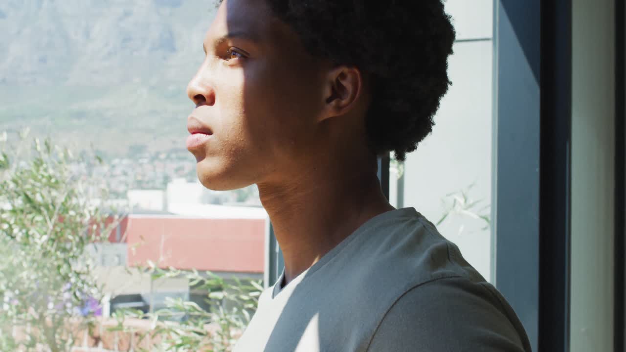 hombre afroamericano mirando por la ventana y bebiendo café en casa