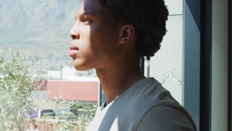 hombre afroamericano mirando por la ventana y bebiendo café en casa