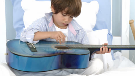 close up of little boy playing guitar on bed
