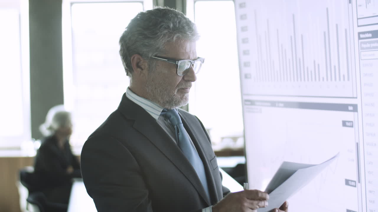 Content bearded businessman checking papers with data on screen