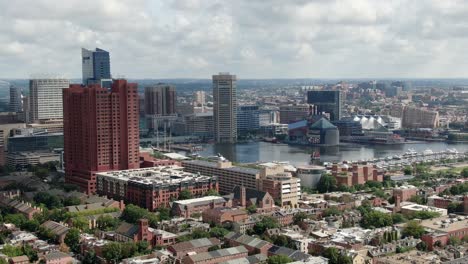 rising aerial establishing shot as clipper ship sailboat enters inner harbor in baltimore maryland usa on summer day, city urban skyline under beautiful clouds, neighborhood ocmmunity houses below