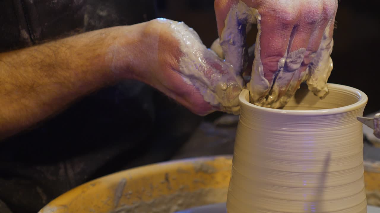Close-up of artisan potter hands molding wet clay on a spinning wheel. Ceramicist creating a vessel using traditional craftsmanship techniques in a workshop