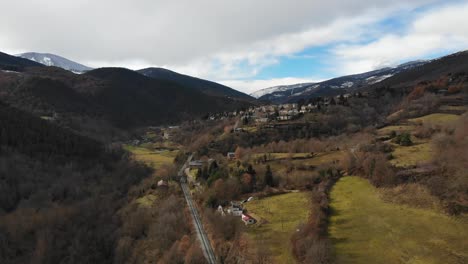 aerial: approaching a little mountain town in a mountainous landscape with snow covered mountains in the background