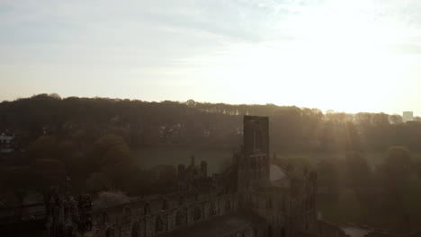 aerial tracking shot of kirkstall abbey at dawn with lens flare on sunny spring day facing sun