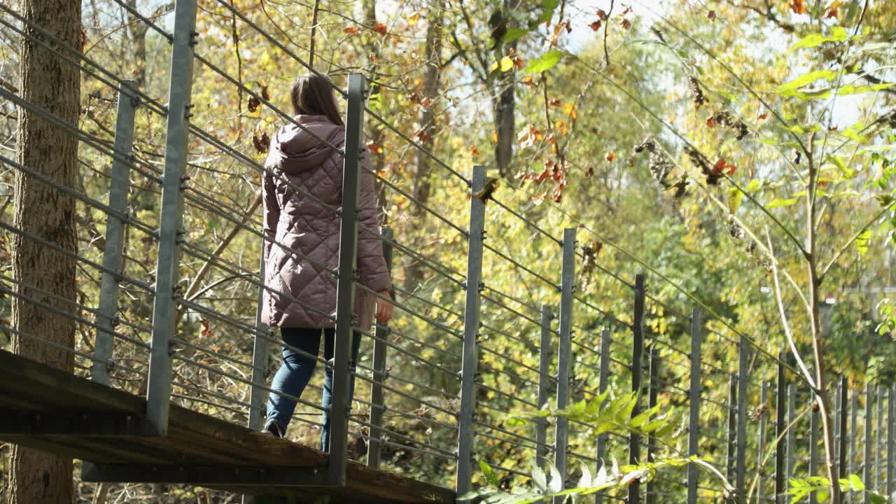 una chica guapa con una chaqueta morada cálida y acogedora cruza un puente colgante durante la temporada de otoño y explora con asombro
