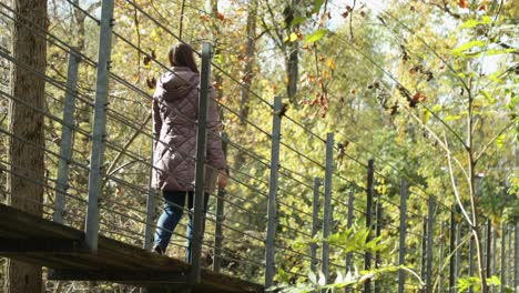 pretty girl in a purple warm cozy jacket walks across a suspension bridge during the autumn season and explores in wonder