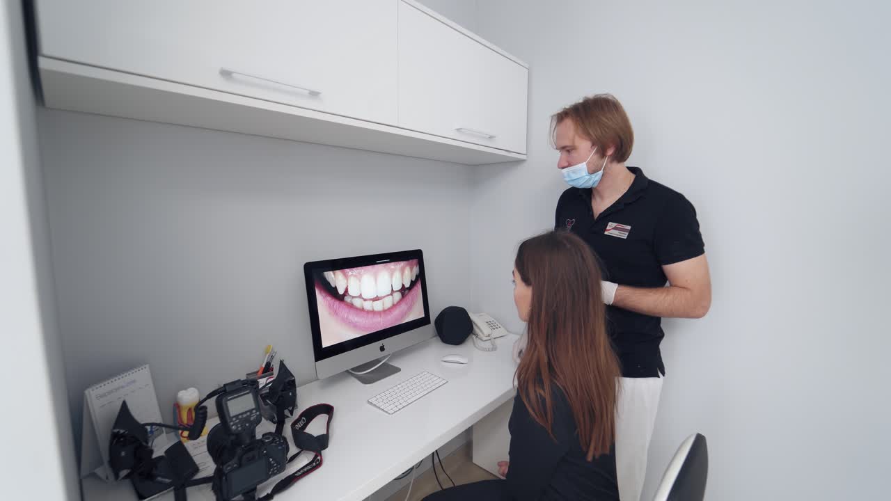 Young woman looking at her teeth on a screen. Dentist showing to a female patient photo of her smile on the monitor on the modern medical room background.