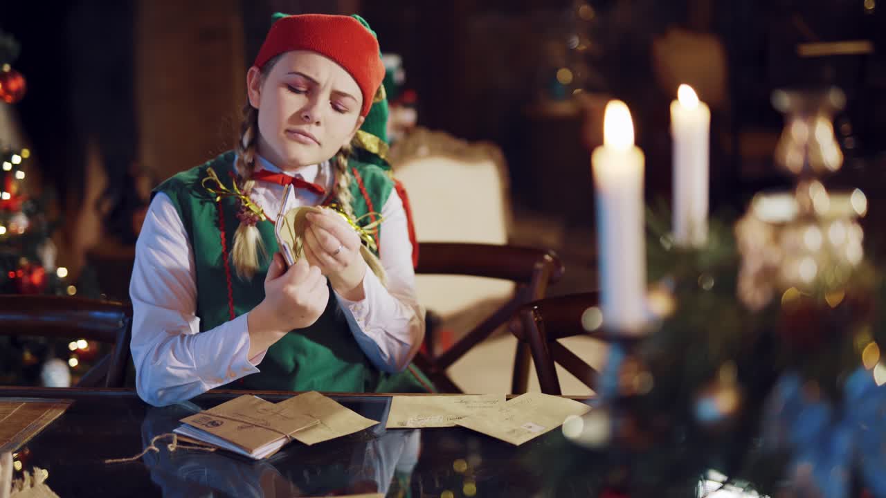 A jolly elf looks through a stack of envelopes with wishes and happily dances against the background of candles and a fireplace in the room. Mail for Santa Claus