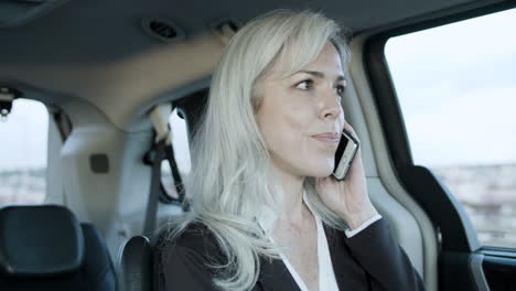 gray haired businesswoman talking on phone inside a car