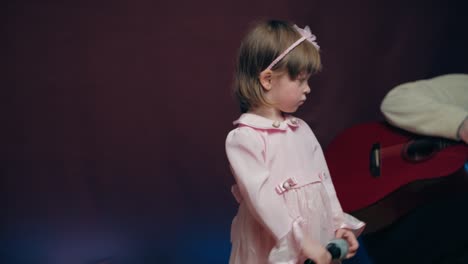 cute little girl in a pink vintage dress stands with a microphone on stage