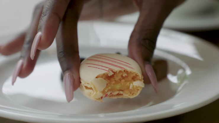 An attractive woman picks up a delicious macaroon cookie and takes a bite