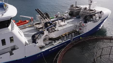 dynamic drone shot of a fishing vessel docked to a fish farming cage