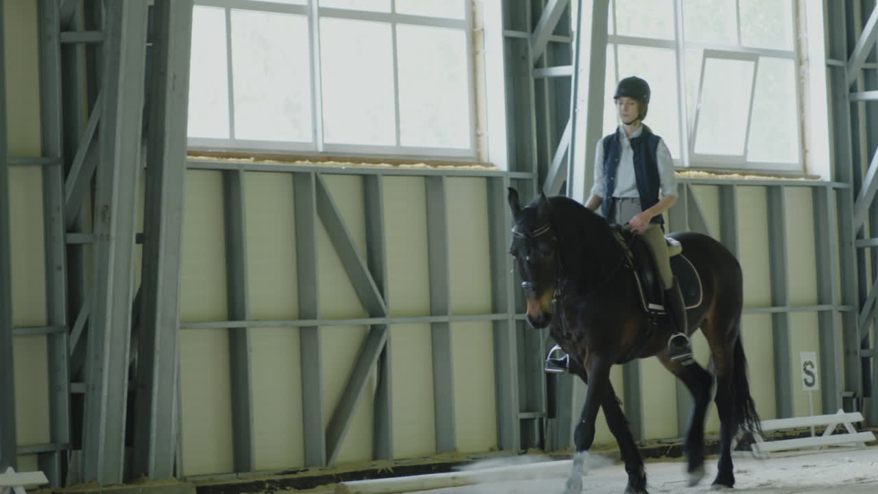 A young person rides a horse in an indoor equestrian arena