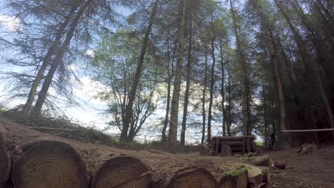 Mountain-Biker-riding-high-speed-in-forestry-track,-over-jump-onto-log-path