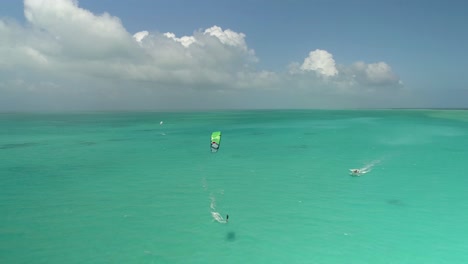 Man-kitesurf-turquoise-caribbean-sea-water,-aerial-Landscape-with-boat-in-the-middle-of-the-sea