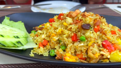 Squeezing-lemon-on-spicy-fried-rice-with-chicken,-vegetables,-crispy-onion-and-cucumbers-at-a-Thai-restaurant,-tasty-traditional-asian-food,-4K-shot