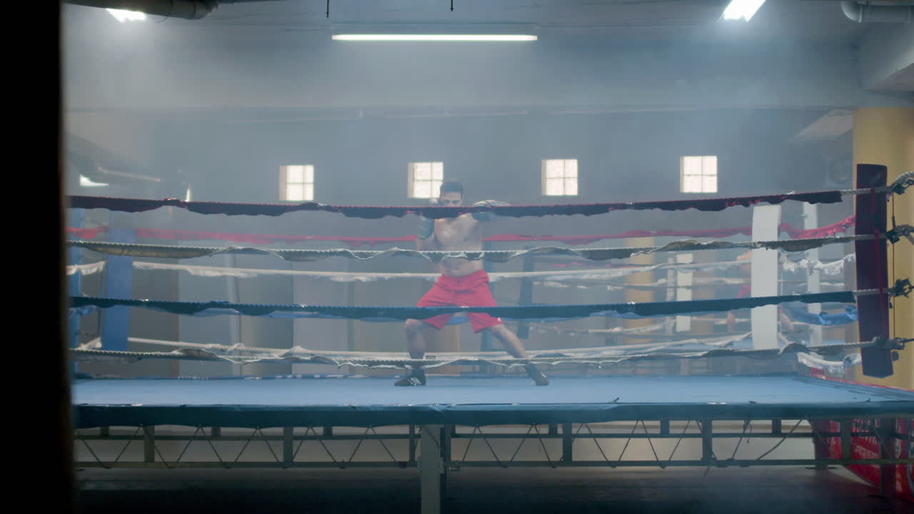 Strong male athlete doing shadow fight in boxing gym