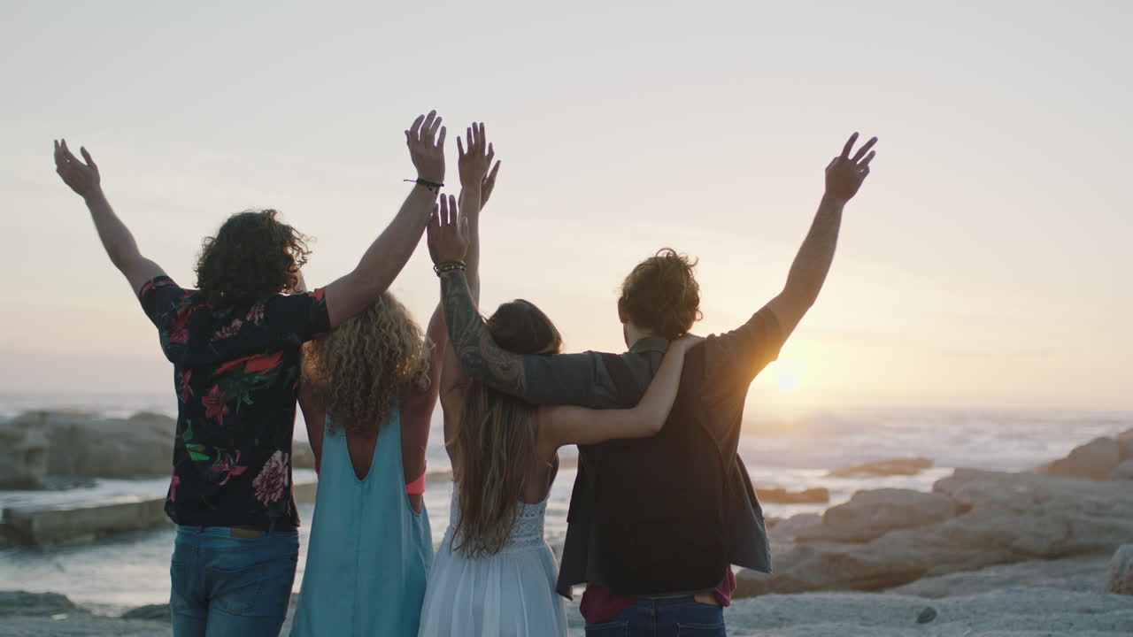 amici sulla spiaggia che si abbracciano festeggiando con le braccia alzate un bel tramonto