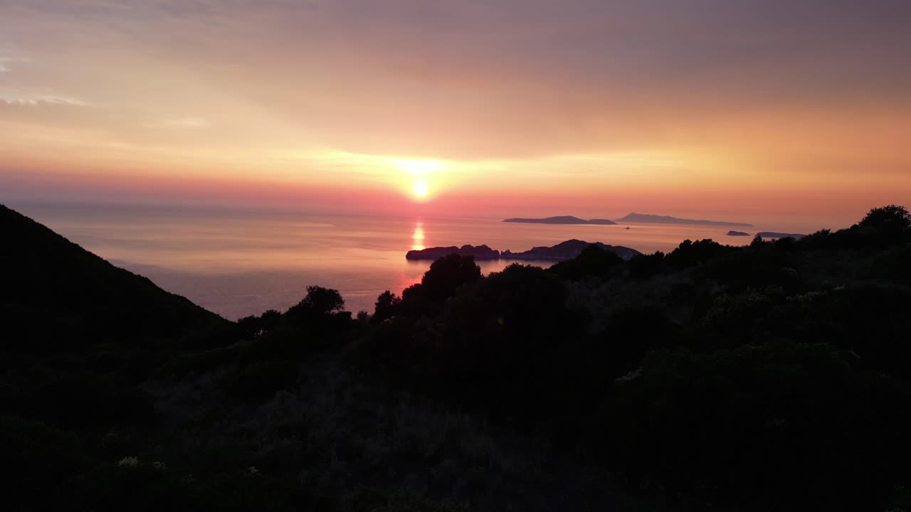 Aerial cinematic drone captures a mountain’s silhouette against the setting sun and sea, creating a dramatic sense of vastness across the horizon.
