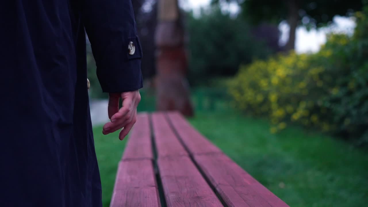 Close up shot of woman's hand wearing black jacket and walking along a wooden bench in a park during evening time