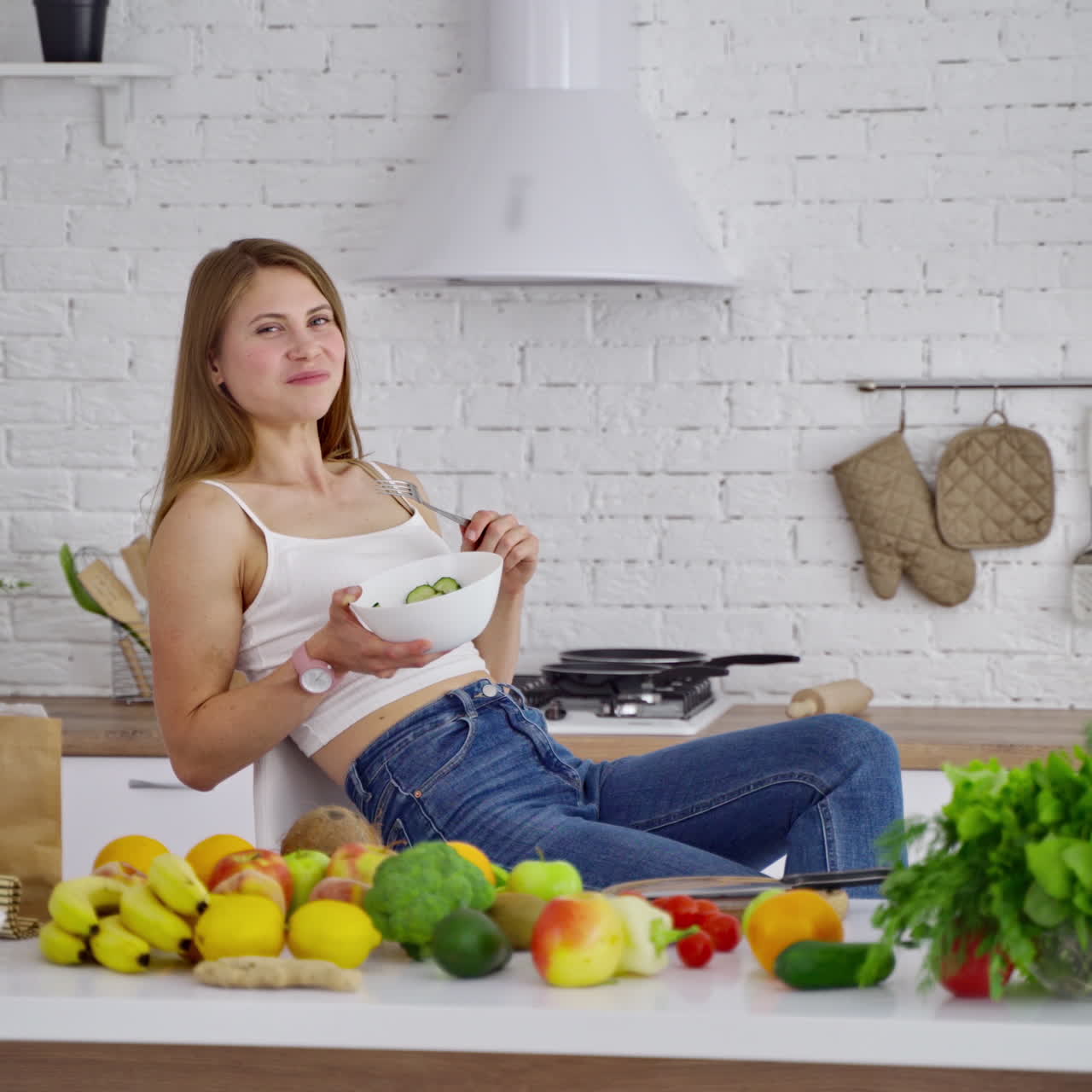 Smiling woman eating healthy food. Beautiful young lady sitting in the kitchen and eating salad on fresh organic food background.