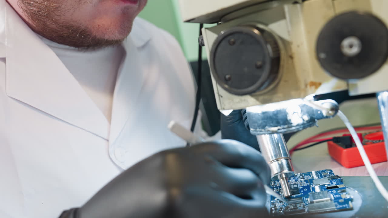 A close-up view of a technician in a laboratory, focusing intently on a circuit board under a microscope as he work on the circuit