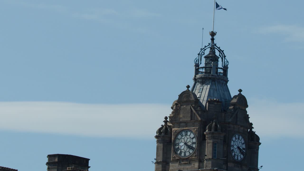 Victorian clock tower with Scottish flag waving, clear daylight, static camera, blue sky background