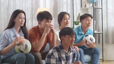 asian teenagers cheering and watching football game on tv and disappointed at home