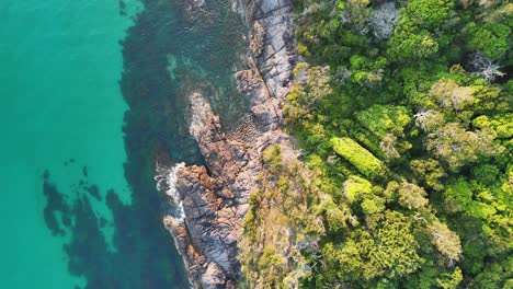 Impresionante-Vista-Aérea-De-Una-Prístina-Cala-Turquesa-Rodeada-De-Un-Terreno-Costero-Escarpado-Y-Una-Exuberante-Vegetación.