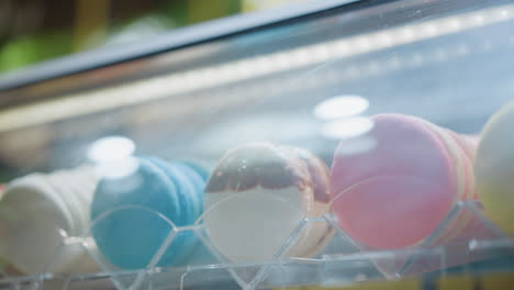 close-up of vibrant macarons displayed in a glass case with reflective lighting, showcasing a colorful assortment of yellow, green, white, and blue macarons