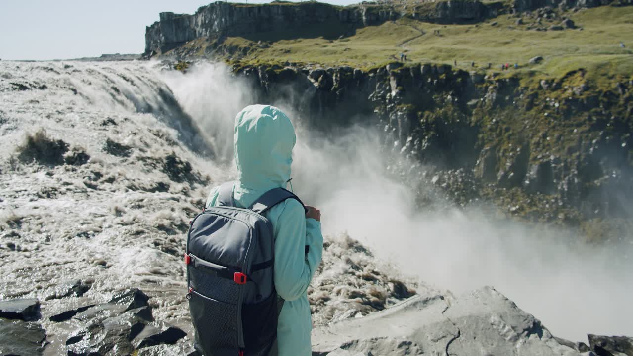 mujer de pie en el borde del acantilado disfrutando de la remota cascada de detifoss en islandia