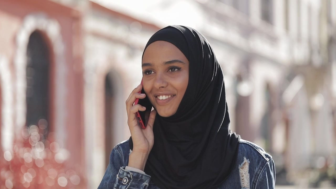 Ung kvinde med hijab taler i smartphone udendørs