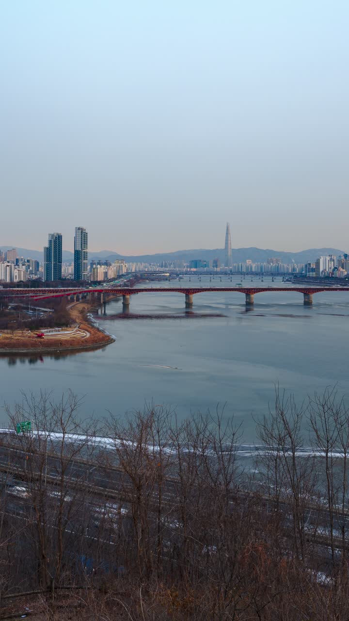 Hyperlapse verticale che attraversa Seul in inverno rivelando il traffico intenso sull'autostrada Gangbyeonbuk-ro, il tranquillo fiume Han, il ponte Seongsu e la torre Lotte avvolta nella nebbia che si erge sullo skyline